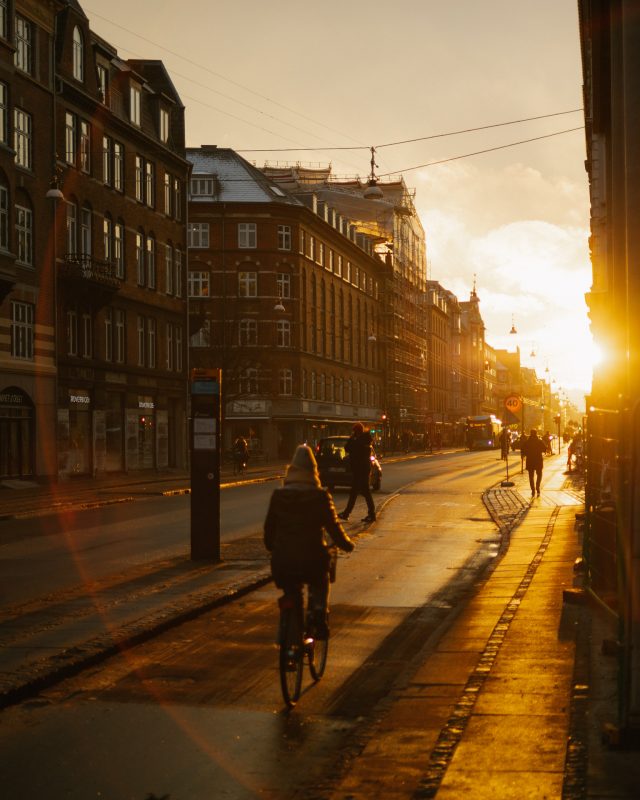 Sonnenaufgang in Kopenhagen, eine Fahrradfahrerin fährt in Richtung der tiefstehenden Sonne