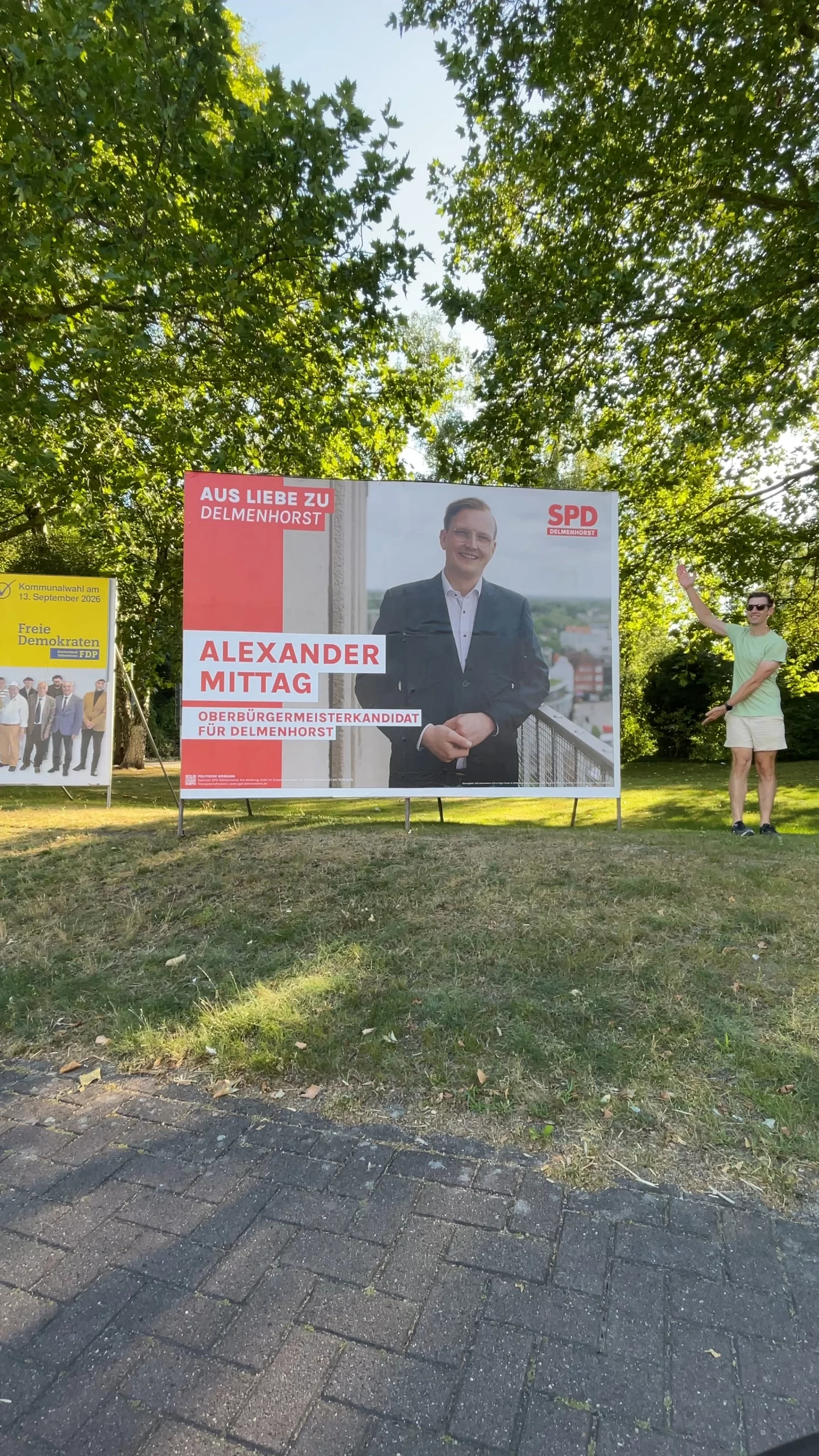 Ich stehe neben einer großen Plakatwand mit der Wahlwerbung für Alexander Mittag.